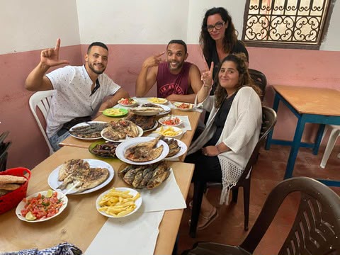 Marouane partageant un repas de poissons grillés avec des voyageurs autour d'une table
